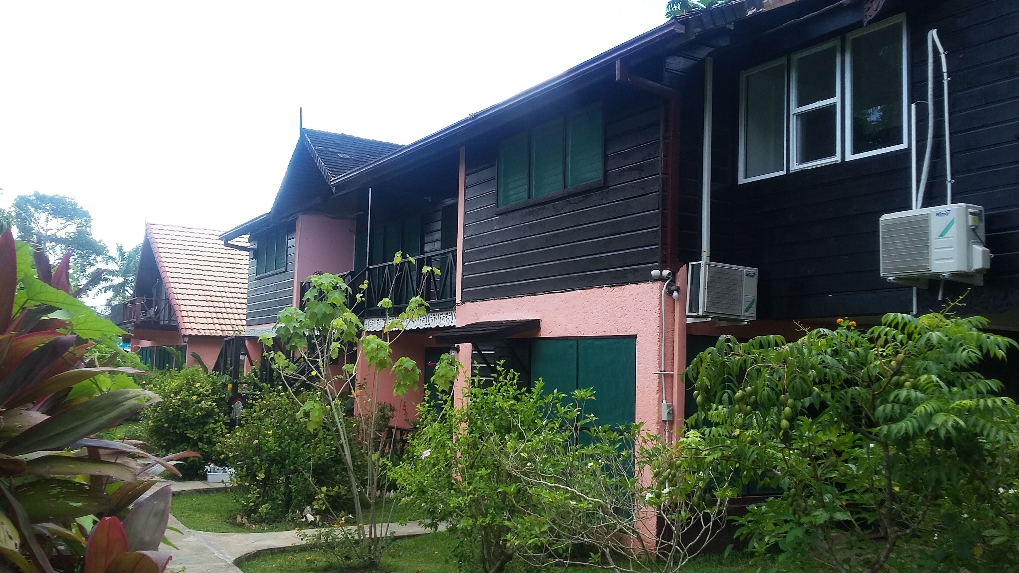 A two-story building with a tiled roof, air conditioning units, and a small garden area with various plants.