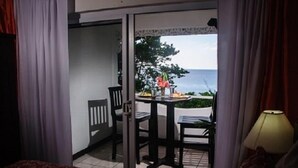 A room with a bed, a table with chairs, and a view of the ocean through a glass door. - Firefly Beach Cottages and Suites (Negril)