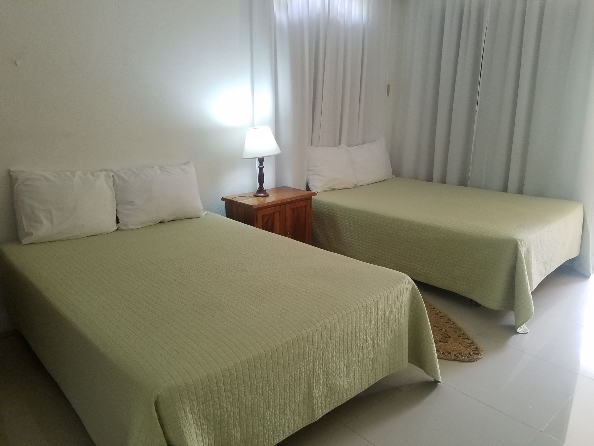 A room with two single beds, a bedside table with a lamp, and a window with curtains.