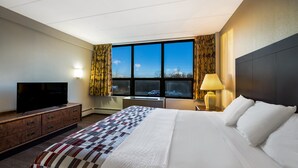 A hotel room with a large bed, a flat-screen TV, a desk, and a window with curtains. - Gateway Inn (Merrick)