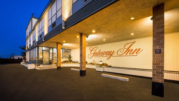 The exterior of Gateway Inn with a prominent entrance, a reception desk, and a sign indicating a parking area. - Gateway Inn (Merrick)