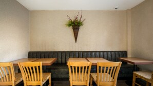 A restaurant interior with wooden tables and chairs, a black cushioned bench, and a potted plant on the wall. - Gateway Inn (Merrick)