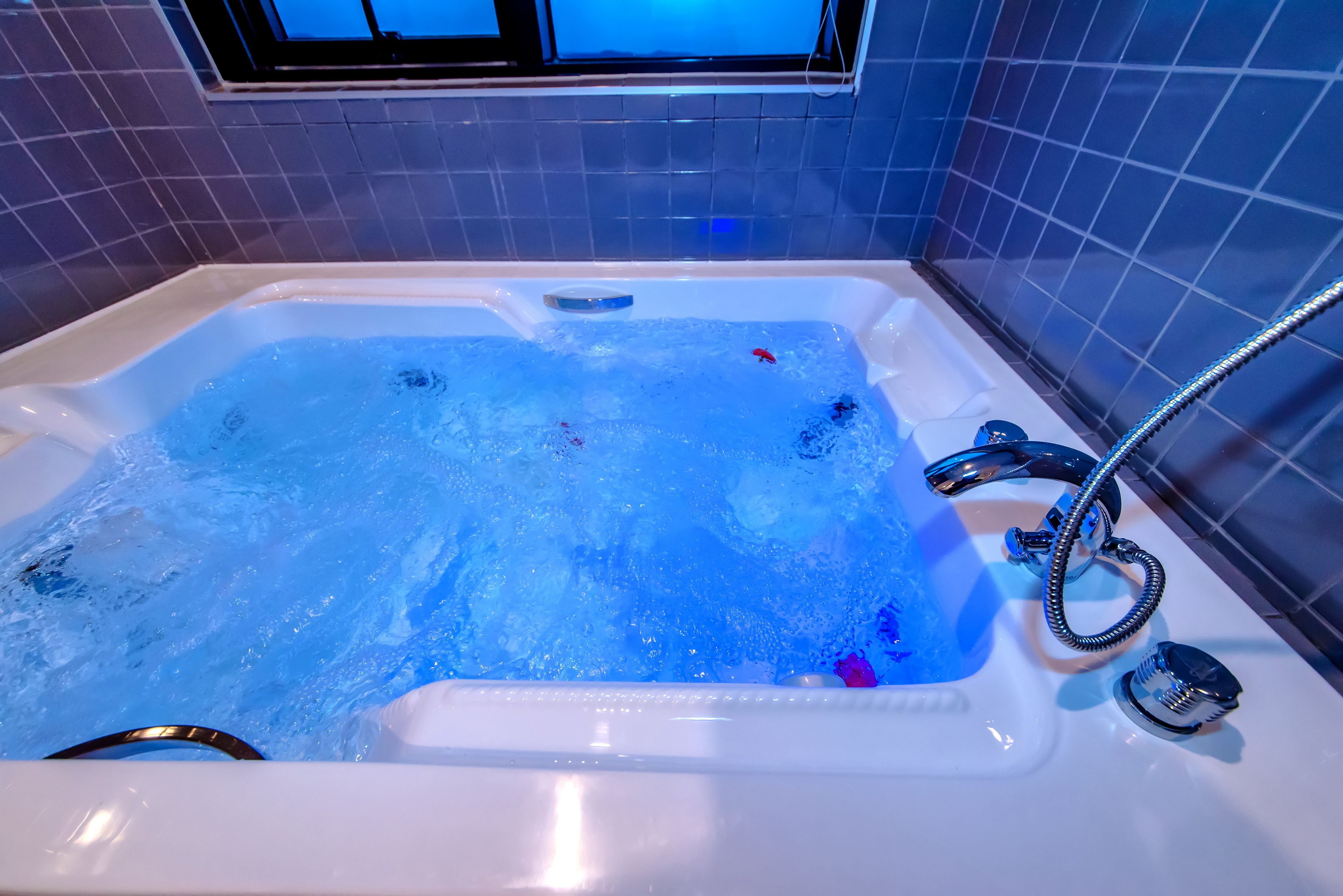 A bathtub with running water, a handheld showerhead, and a window above.