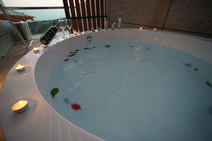 Un jacuzzi con pétalos de rosa flotando en el agua, rodeado de velas y una copa de vino.