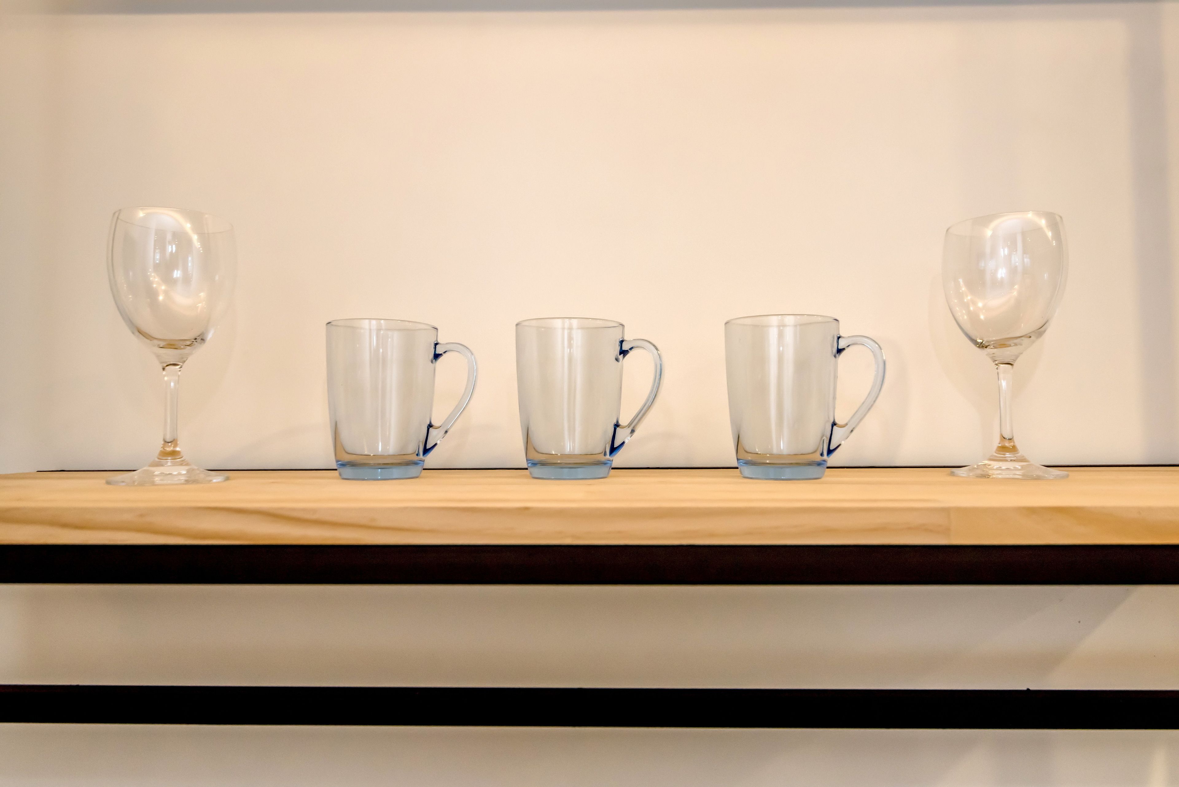A wooden shelf with four clear glass mugs and two wine glasses.