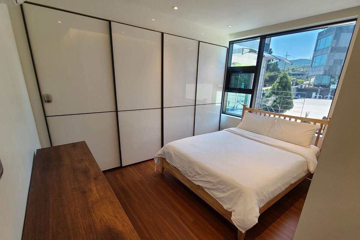 Un dormitorio con una cama, un escritorio de madera y un ventanal grande.
