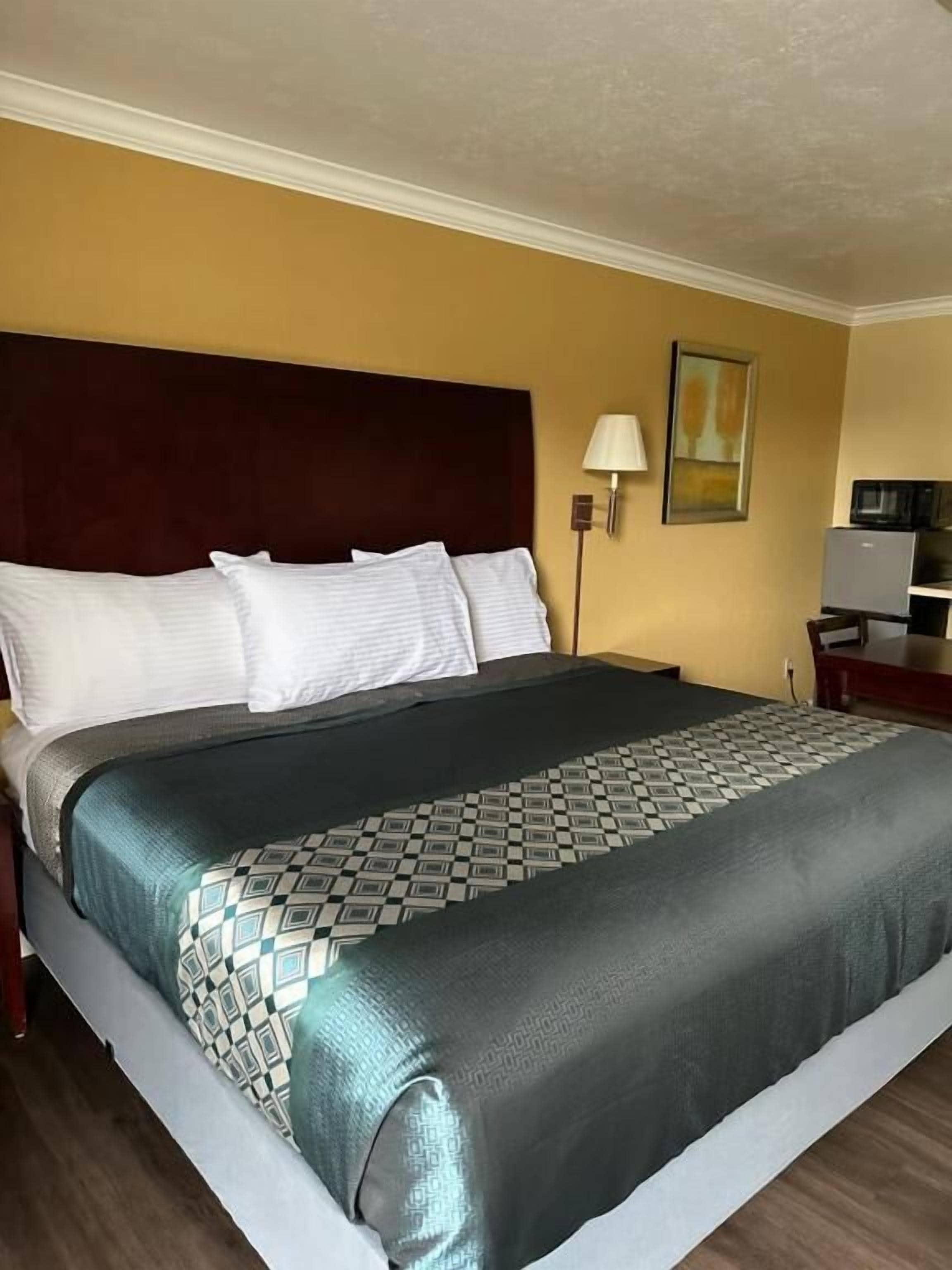 A hotel room with a large bed, a headboard, a bedside lamp, and a small table with a lamp.