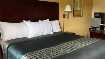 A hotel room with a large bed, a headboard, a bedside lamp, and a small table with a lamp.