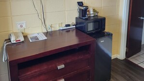 A hotel room with a flat-screen TV displaying 'xfinity', a coffee maker, a microwave, a refrigerator, a wooden dresser with drawers, and a door to the right. - Galaxie Motel (Philomath)