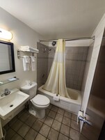 Un baño con lavamanos, inodoro y bañera. Hay un perchero con toallas, una cortina de ducha y un espejo.