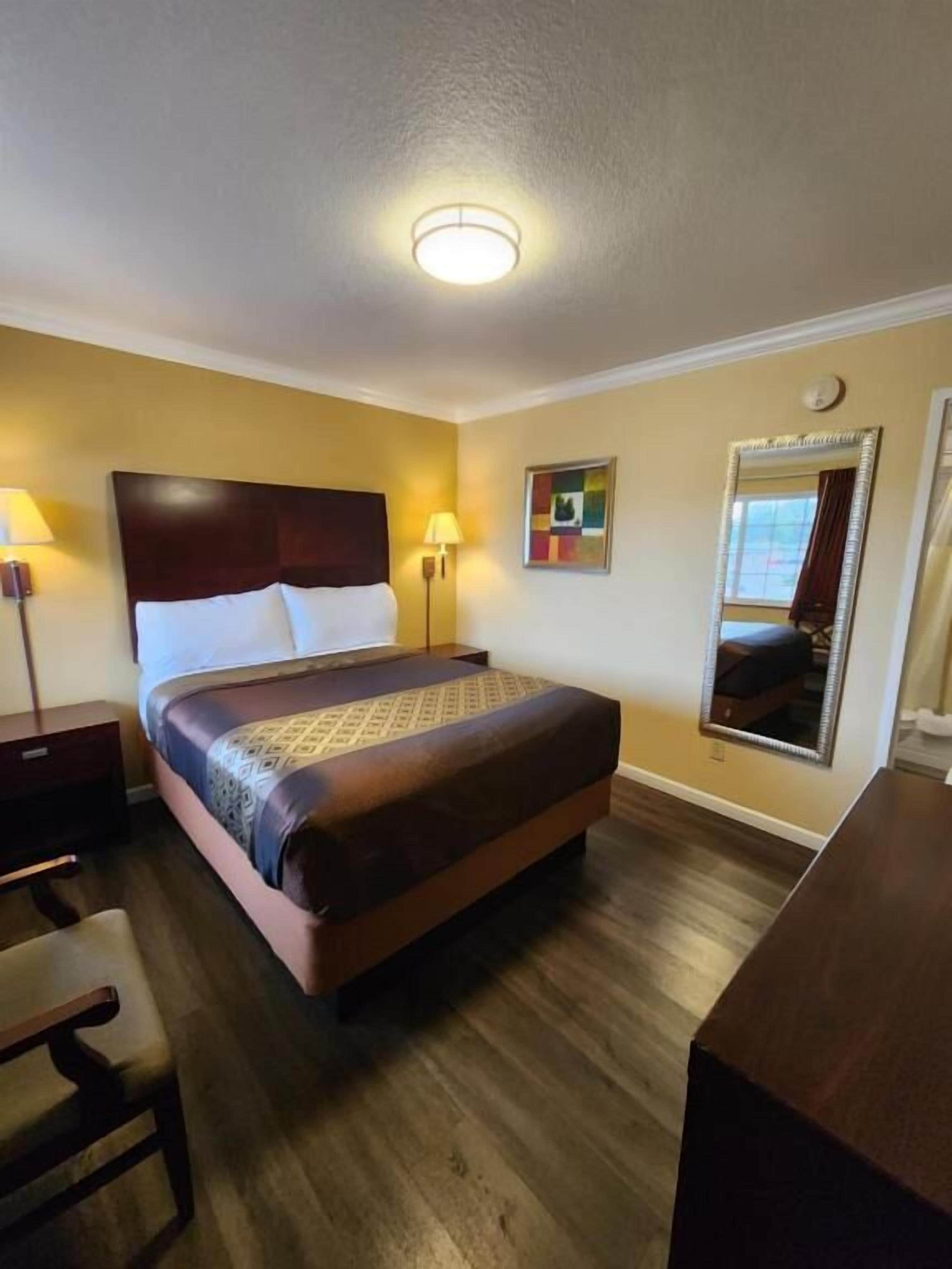 A hotel room with a bed, bedside lamps, a desk, and a mirror.