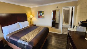 A hotel room with a large bed, a bedside lamp, a mirror, a bathroom with a shower, and a microwave on the counter. - Galaxie Motel (Philomath)