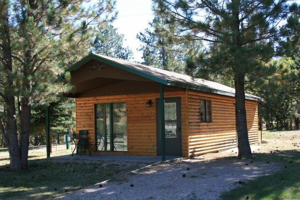 A small wooden cabin with a sliding glass door, a covered patio, and a gravel path.