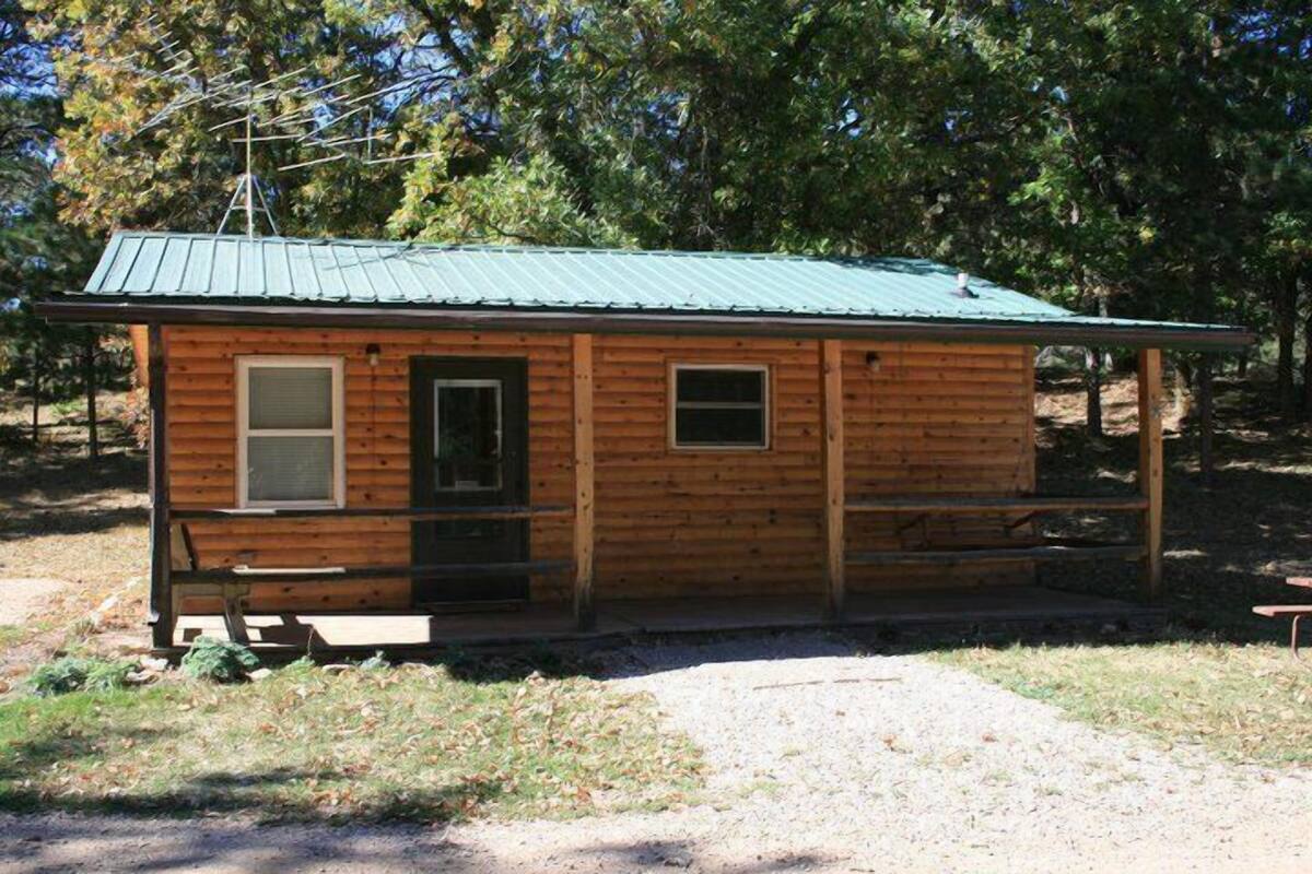 A small wooden cabin with a metal roof, a porch, and a window.