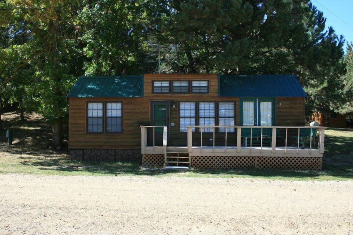 A wooden cabin with a green roof, a porch with a railing, and a stone foundation.