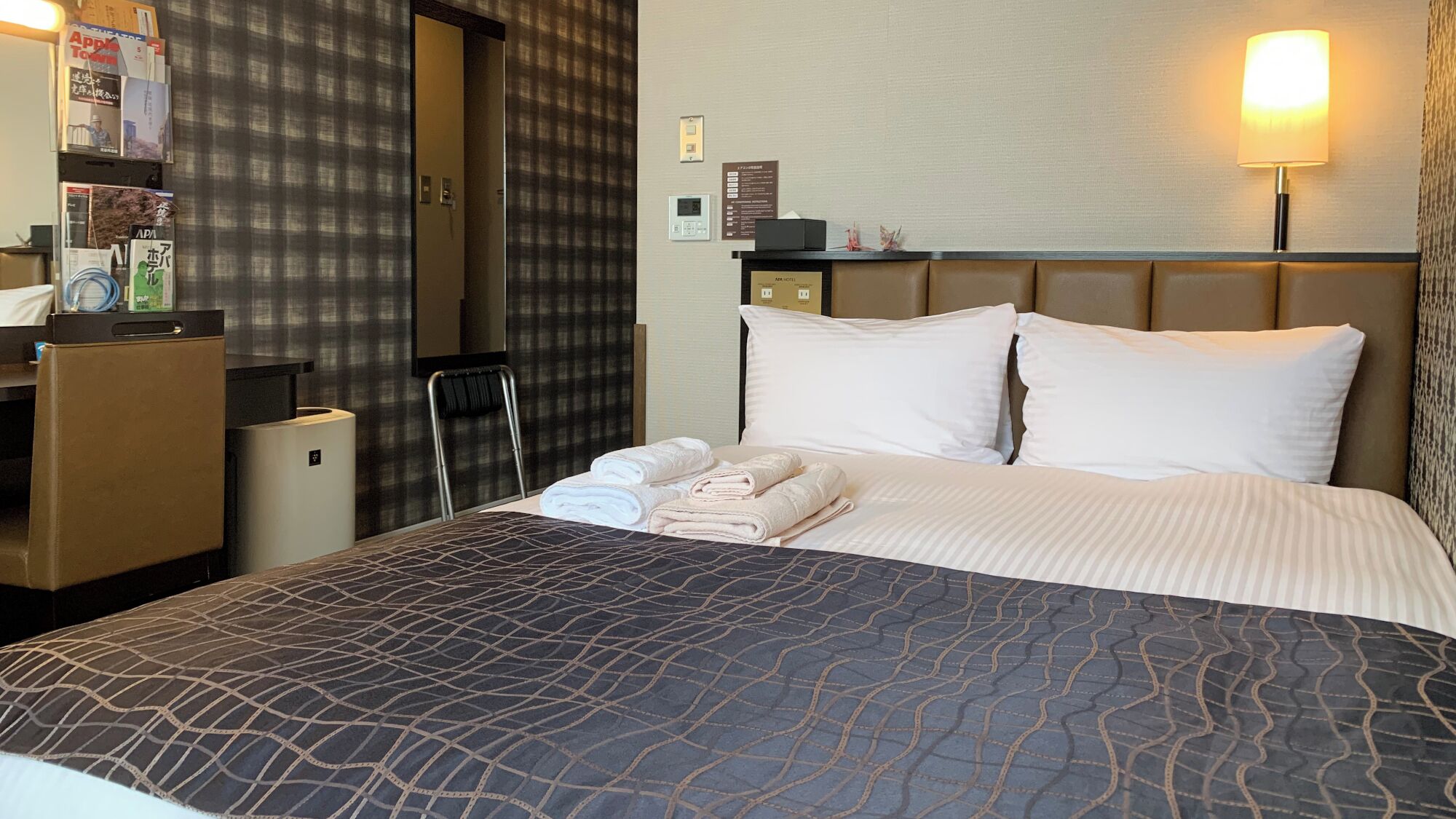 Hotellihuone, jossa on sänky, työpöytä, tuoli, lamppu ja seinälle asennettu televisio.
