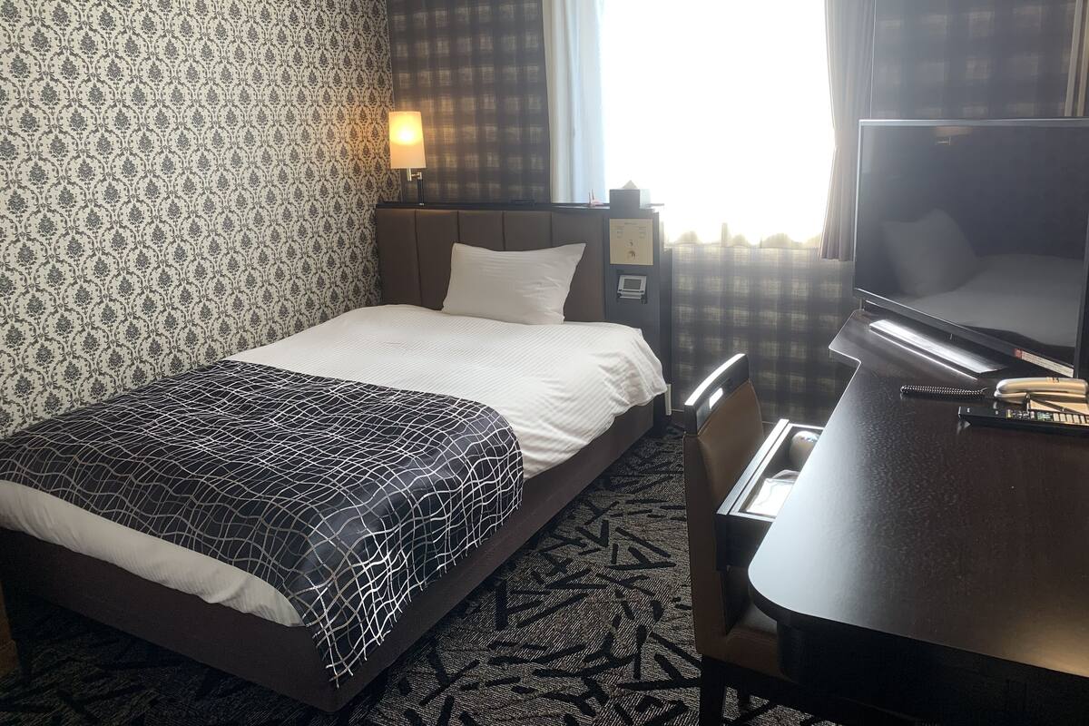 A hotel room with a bed, a desk, a TV, and a window with curtains.