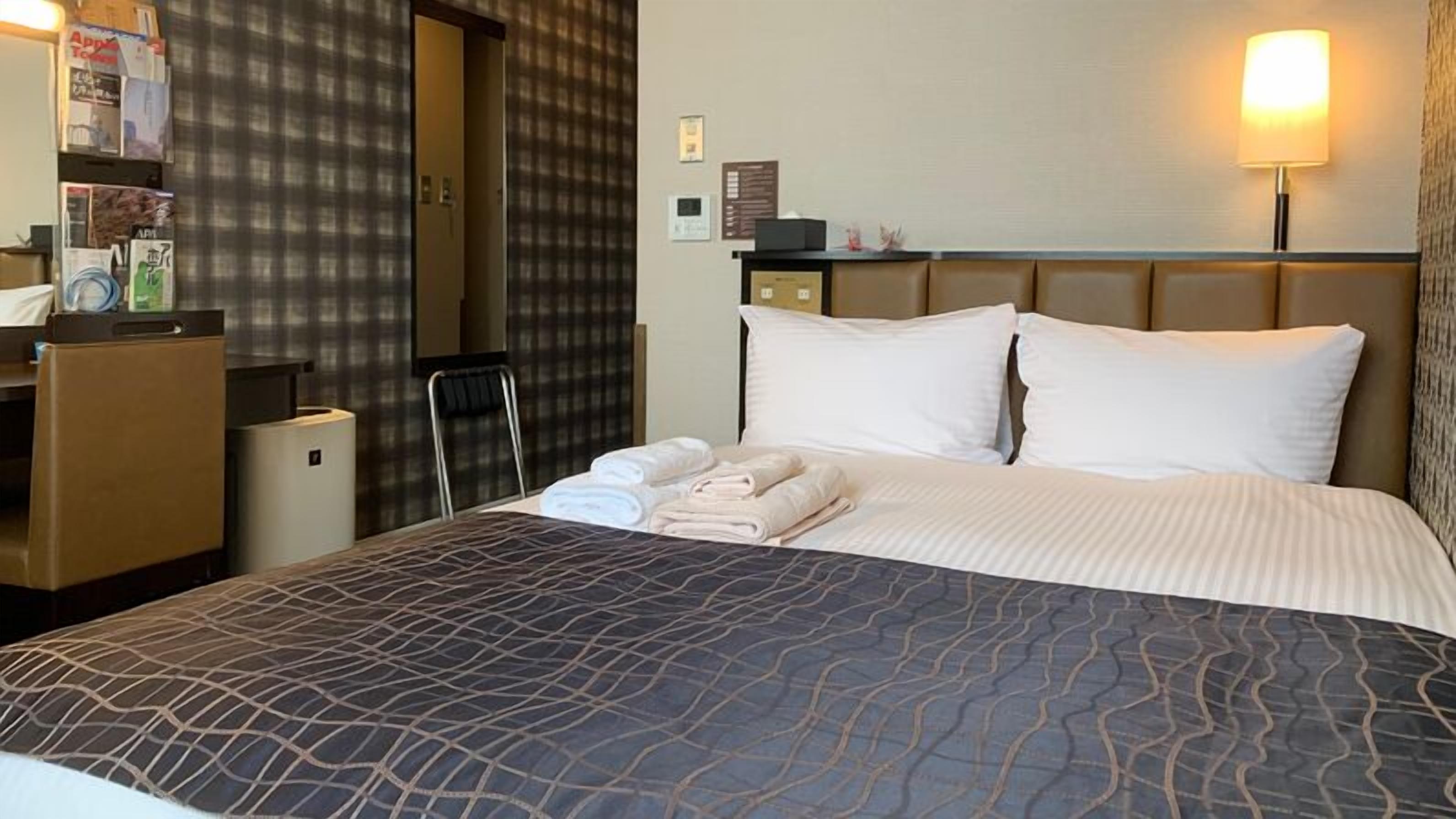 A hotel room with a bed, a desk, a chair, a wardrobe, and a wall-mounted lamp.