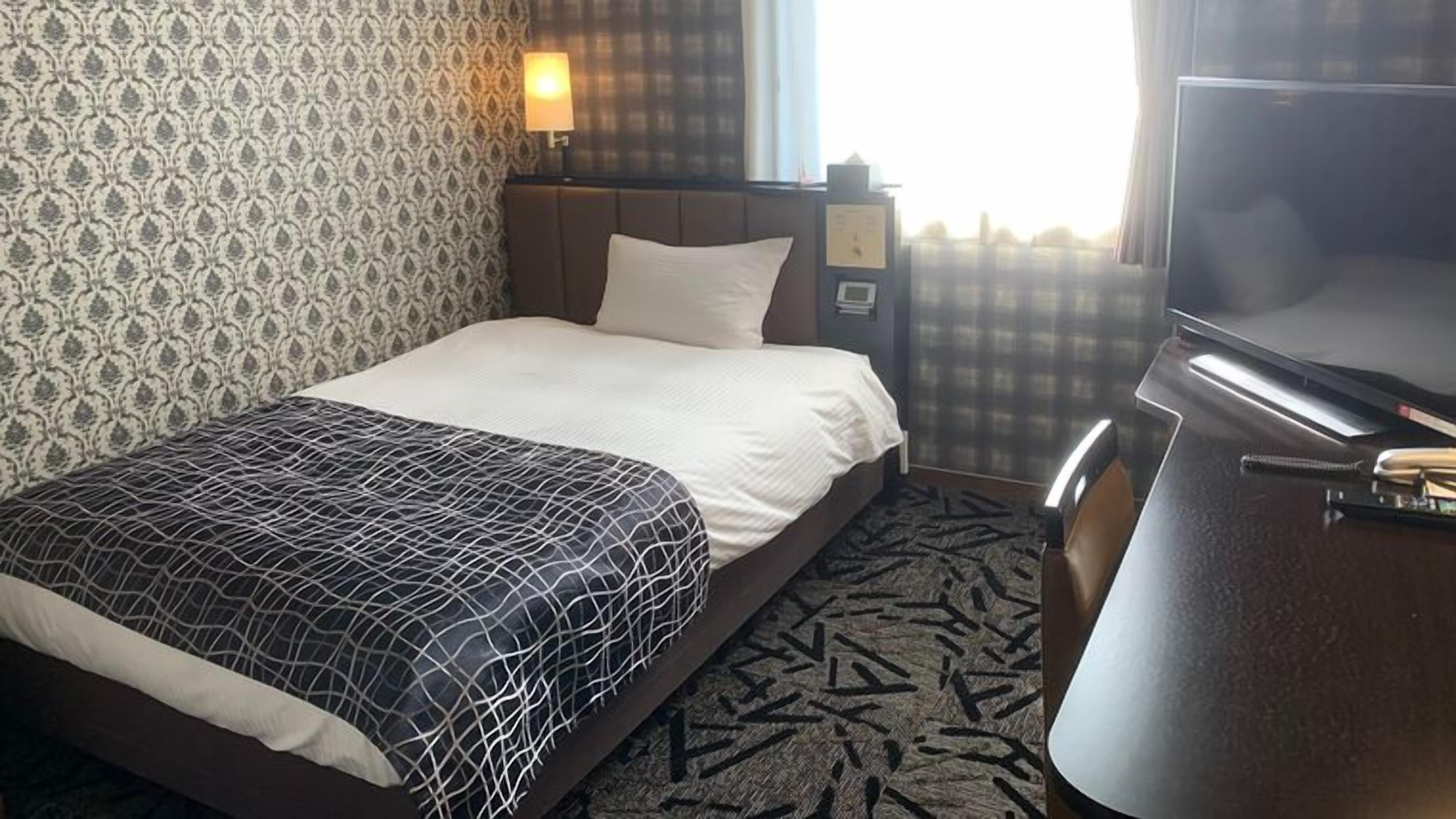 Hotellihuone, jossa on sänky, työpöytä, televisio ja kuviollinen seinä.