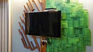 A room with a television mounted on a wooden stand, a green wall with a geometric pattern, and a striped carpet. - Lio Hotel (Taipei)