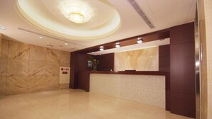 A hotel reception area with a marble wall, a reception desk, and a chandelier. - Lio Hotel (Taipei)