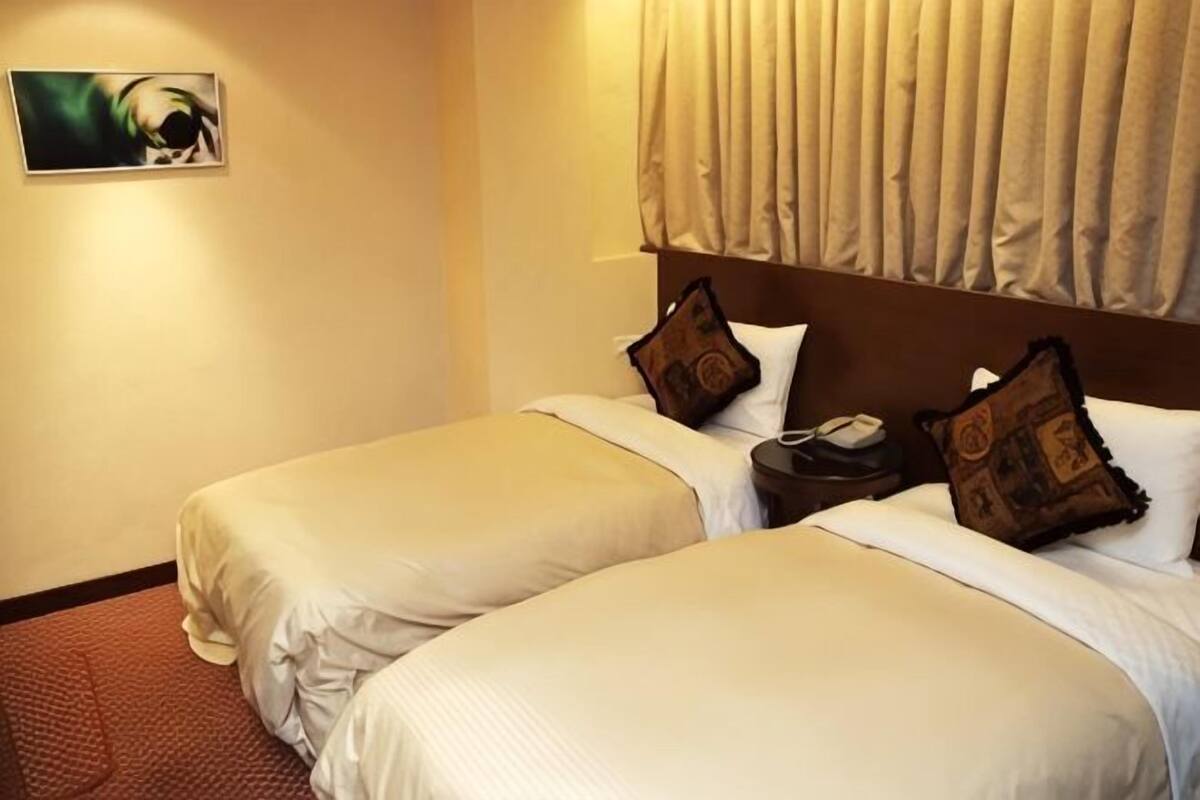 Una habitación de hotel con dos camas, una mesita de noche y un cuadro en la pared.