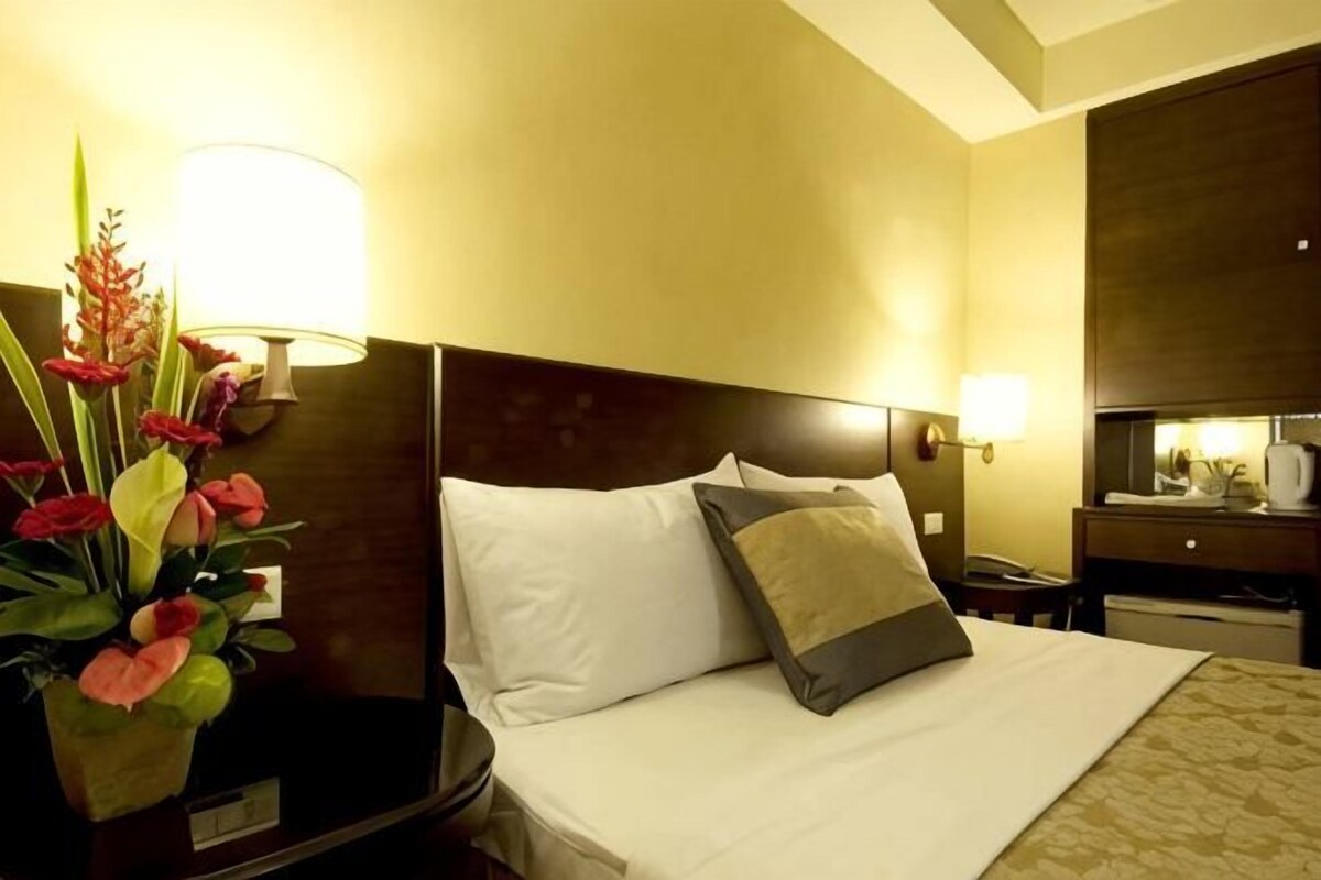 Een hotelkamer met een bed, nachtkastje, lamp en spiegel.