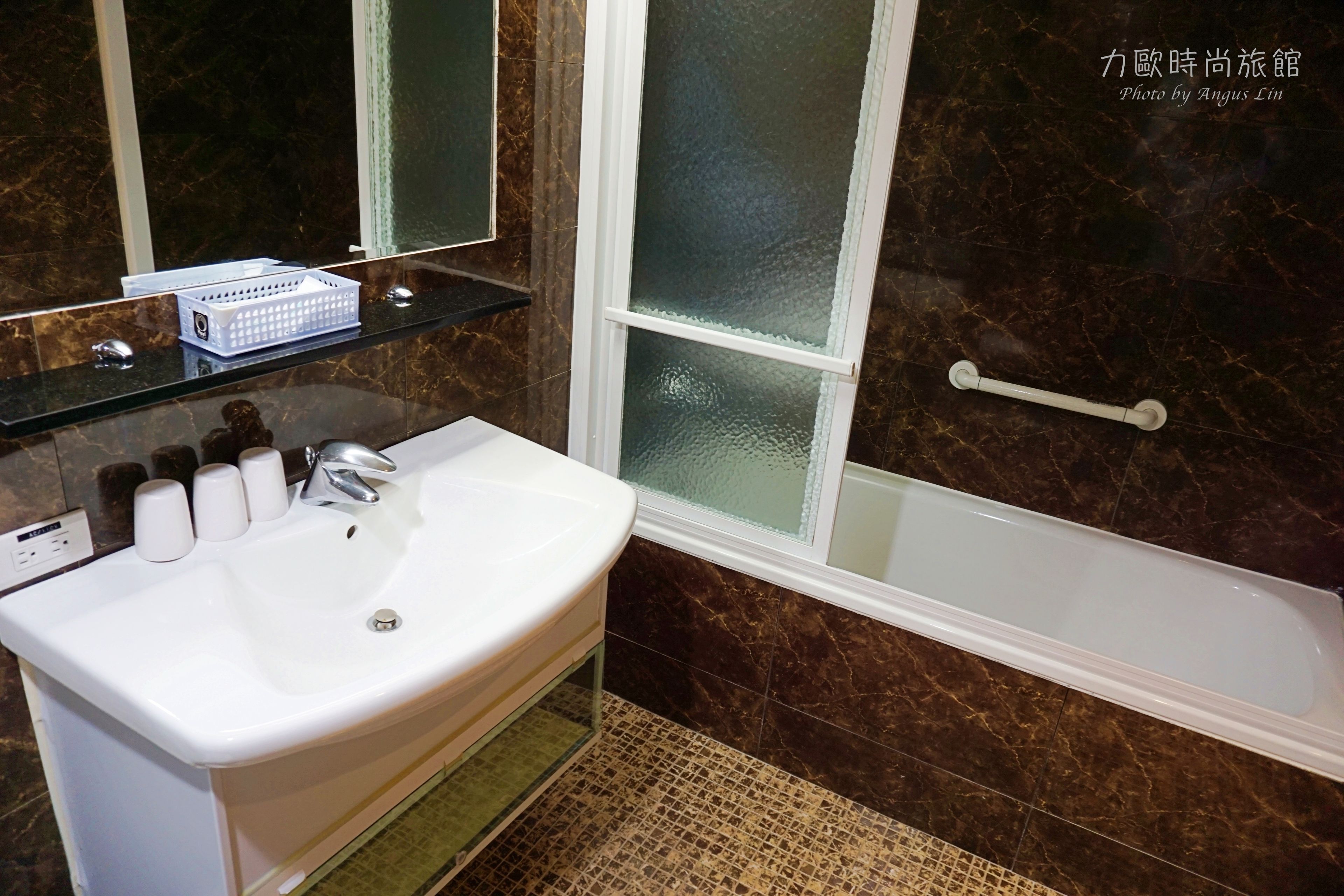 A bathroom with a white sink, a glass shelf with toiletries, a mirror, and a bathtub with a glass door.