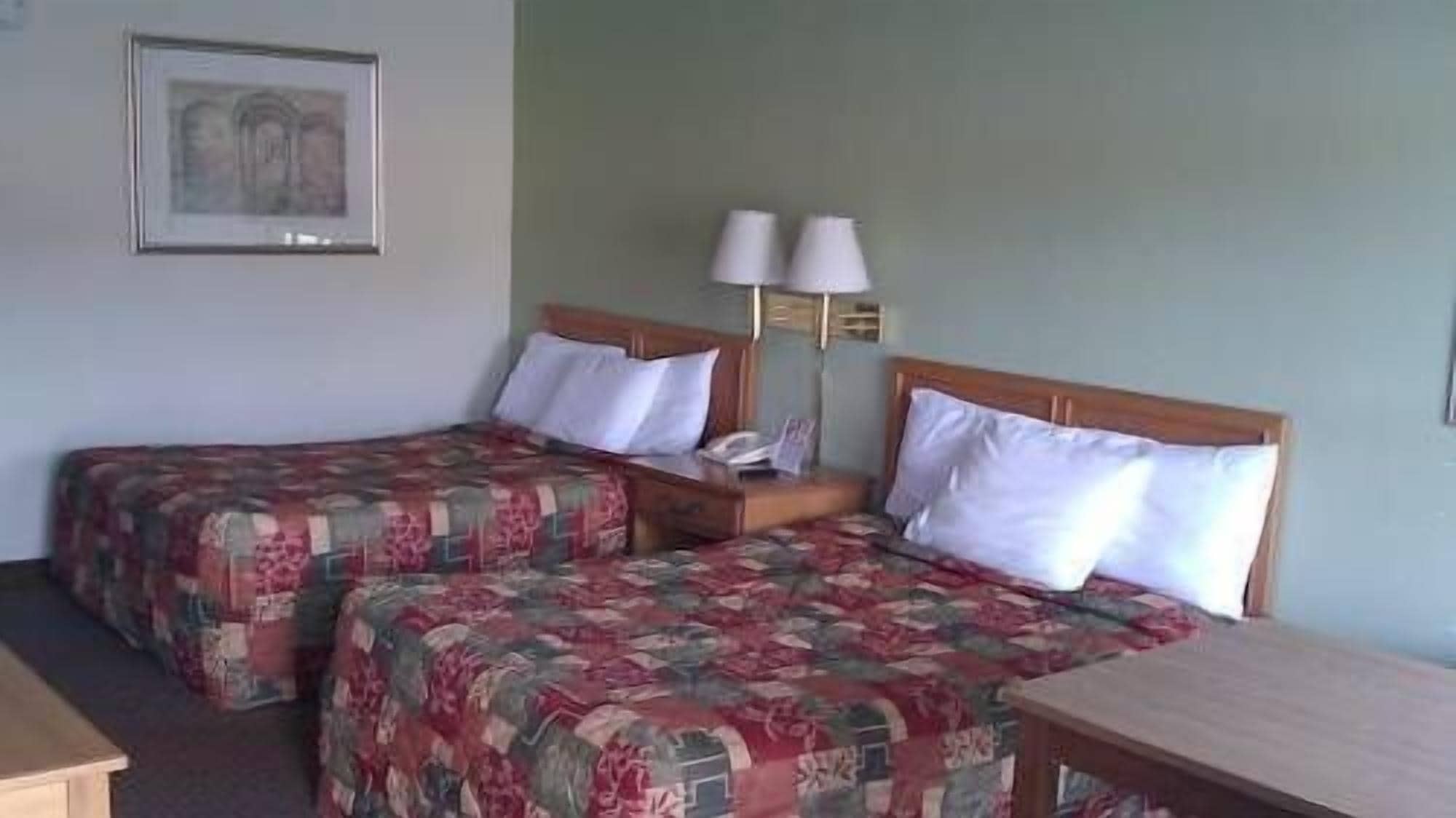 Ein Hotelzimmer mit zwei Betten, einem Nachttisch, einer Lampe und einem gerahmten Bild an der Wand.