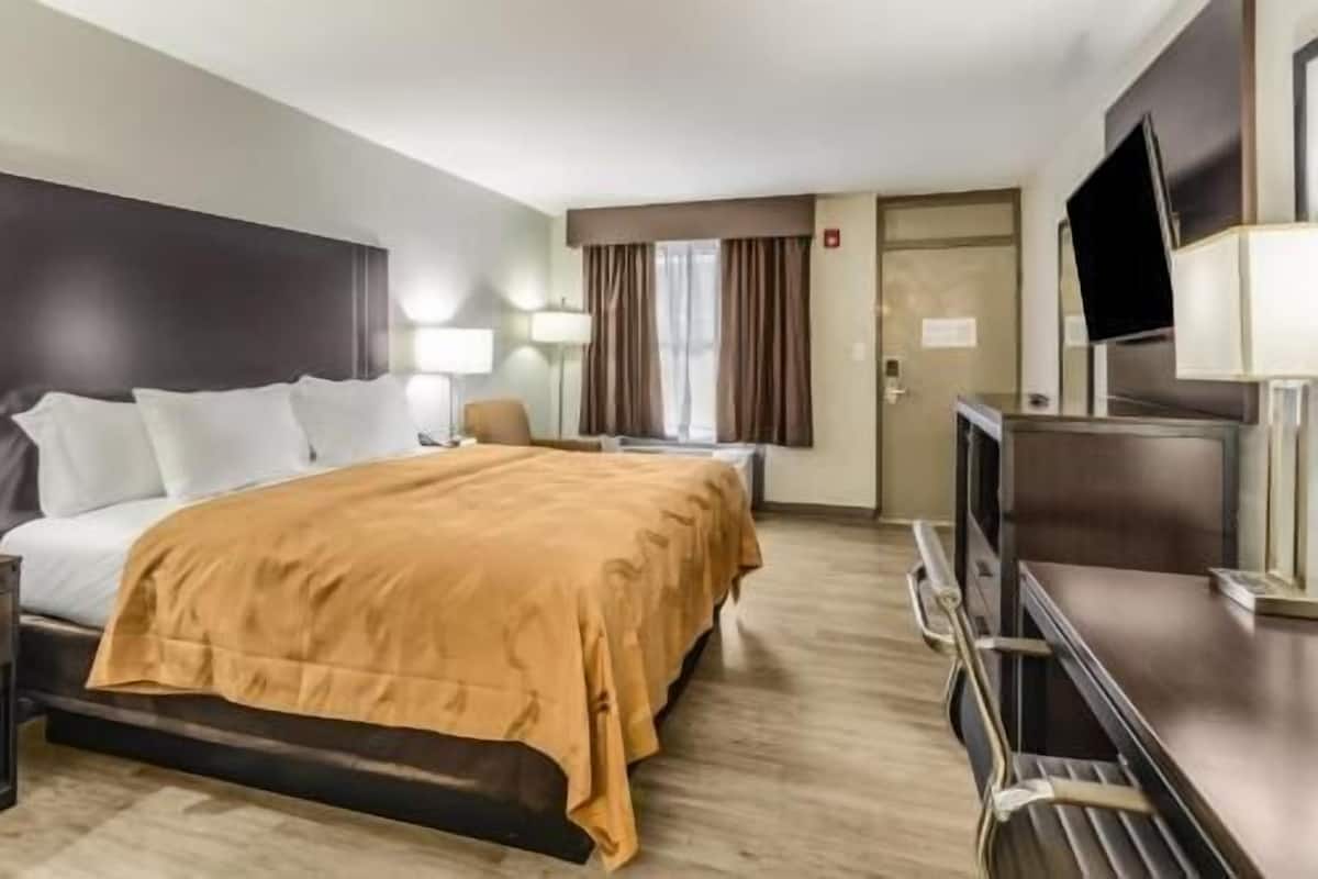 A hotel room with a bed, a desk, a TV, and a door.