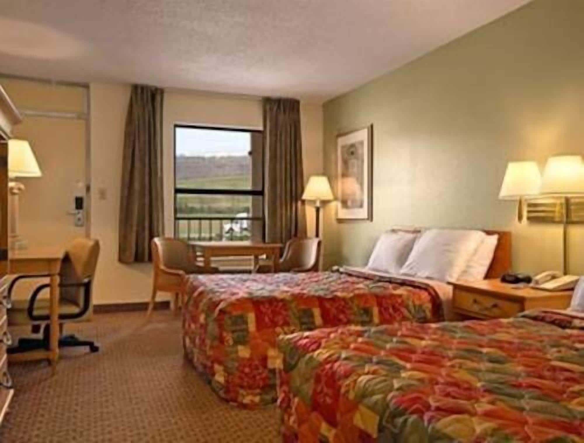 A hotel room with two beds, a desk, a chair, and a window with a view.