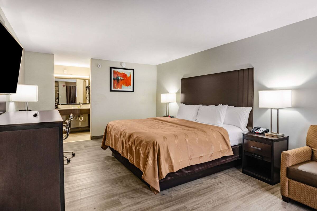 A hotel room with a large bed, two bedside tables with lamps, a desk, and a chair.