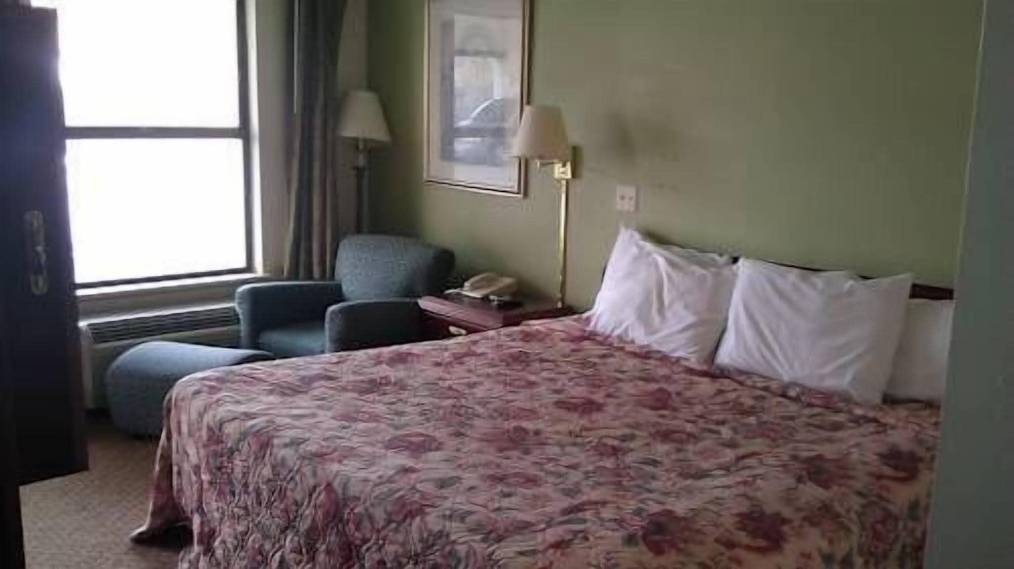 Et hotelværelse med en stor seng, en stol, et skrivebord med lampe og et vindue.