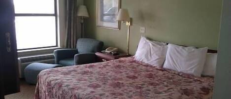 Et hotelværelse med en stor seng, en stol, et skrivebord med lampe og et vindue.