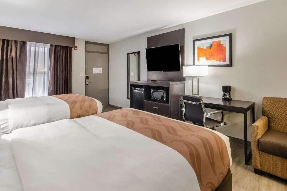 A hotel room with two beds, a desk, a television, a chair, and a painting on the wall.