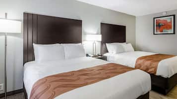 Een hotelkamer met twee bedden, een nachtkastje met een lamp en een lijst met een abstract schilderij aan de muur.