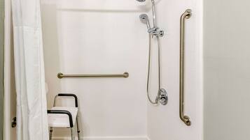 A bathroom with white tiled walls, a shower with a handheld showerhead, a grab bar, and a wheelchair-accessible bench.