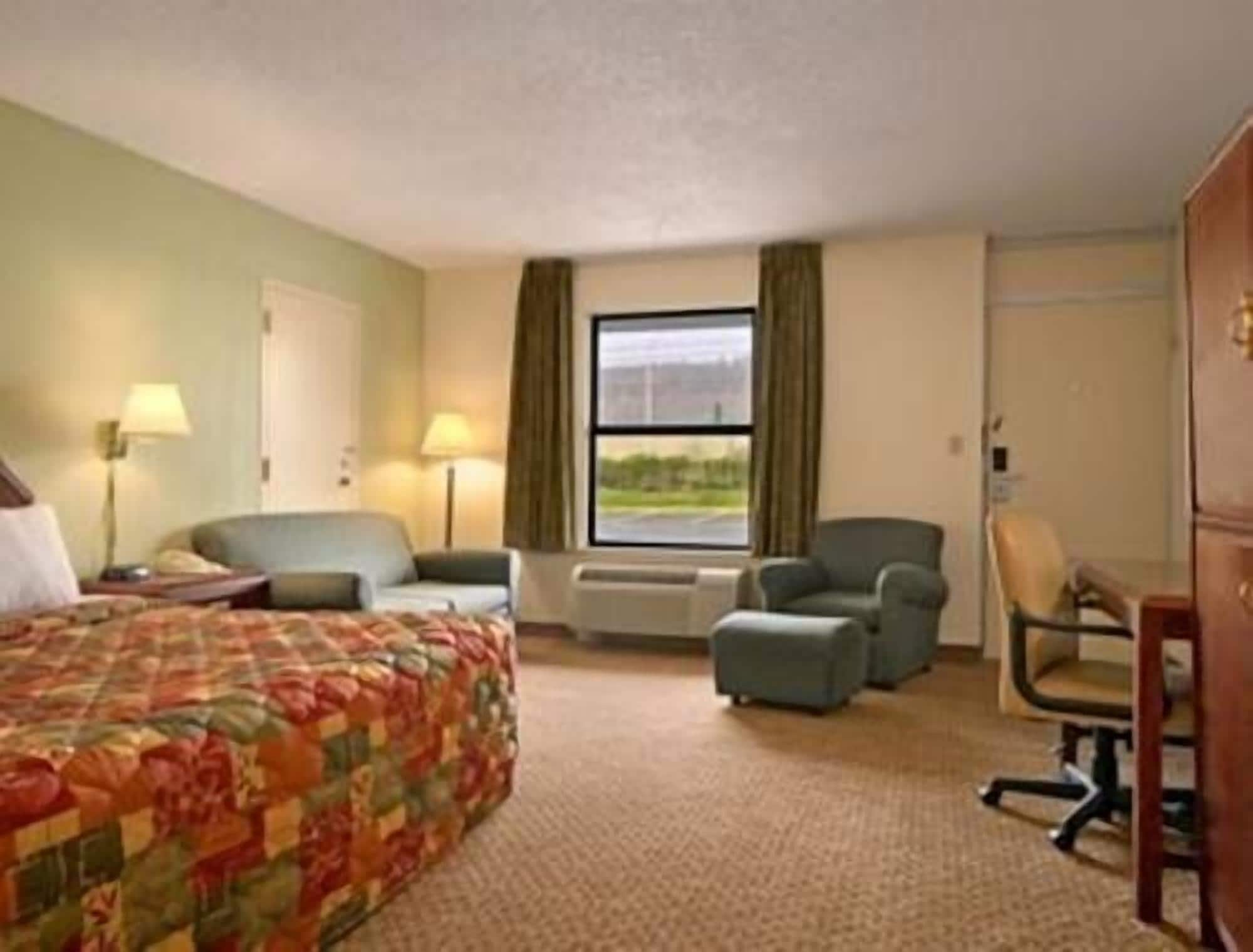 Une chambre d’hôtel avec un lit, deux fauteuils, un bureau et une fenêtre avec des rideaux.