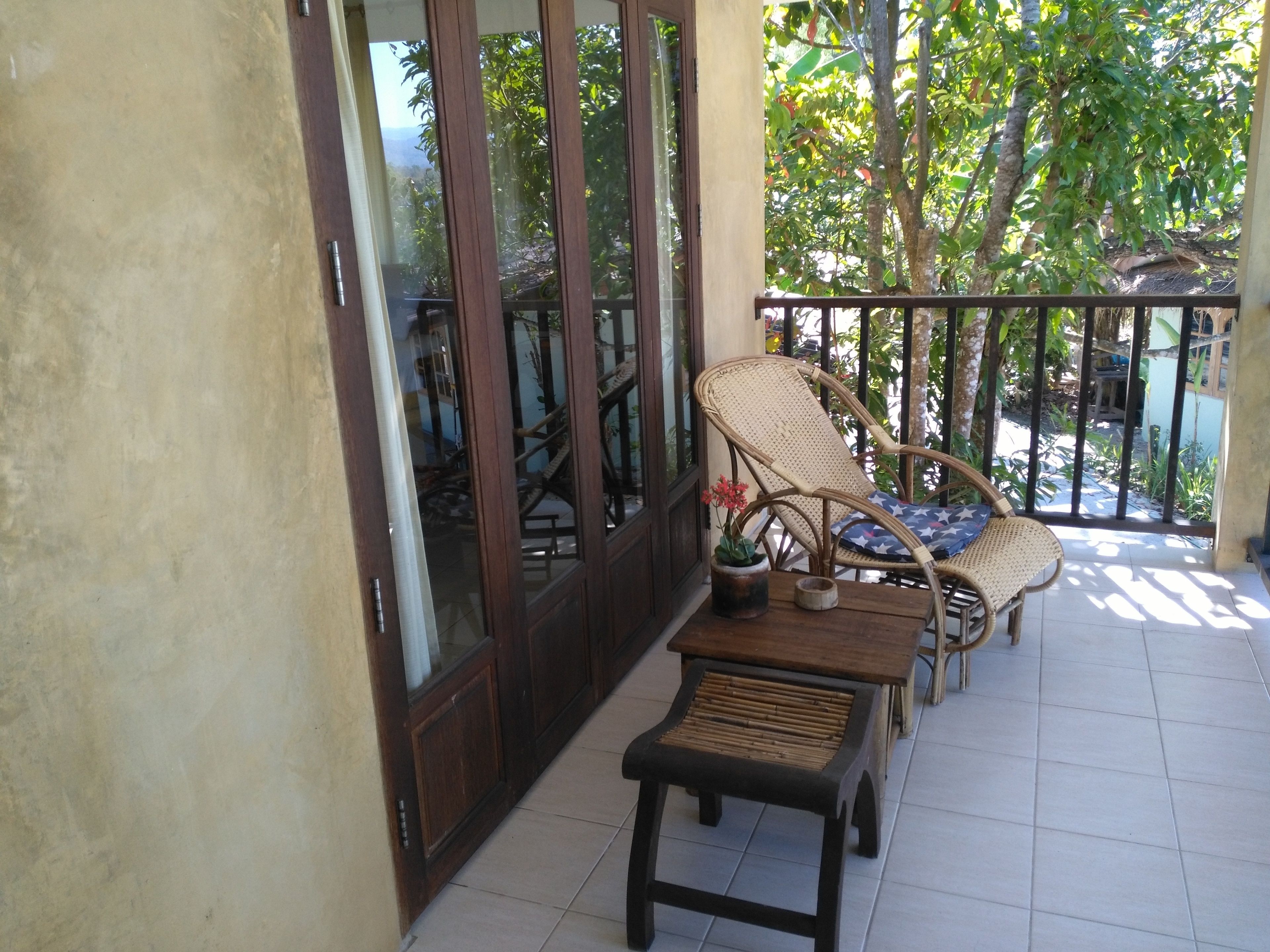 A balcony with two wicker chairs, a small wooden table, and a potted plant.