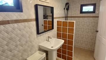Un baño con lavamanos blanco, espejo y zona de ducha.