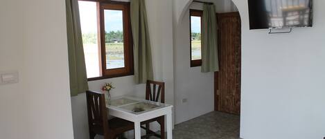 A room with a TV mounted on the wall, a dining table with chairs, and a window with curtains.