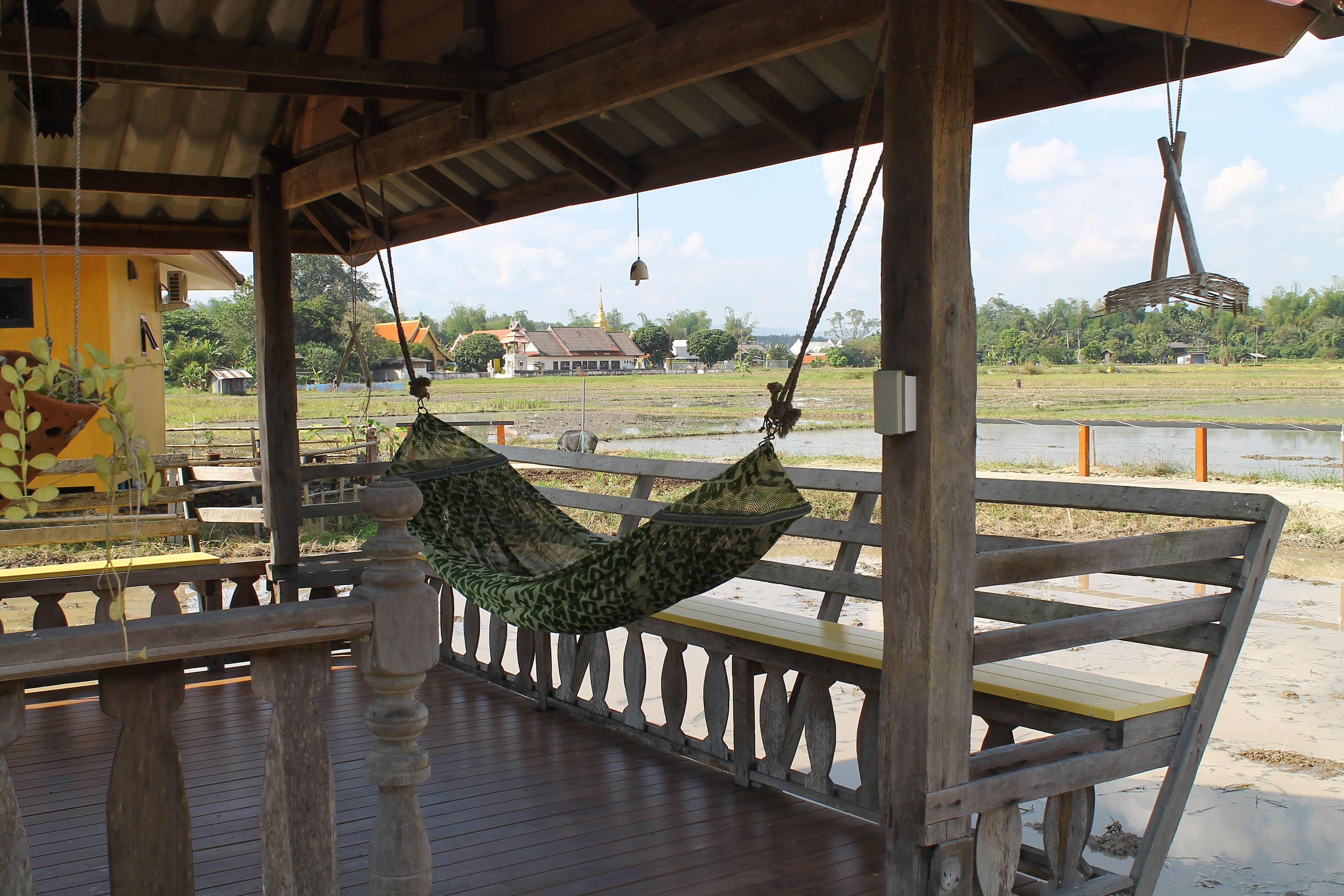 A wooden deck with a hammock and benches, overlooking a water body and buildings in the distance.