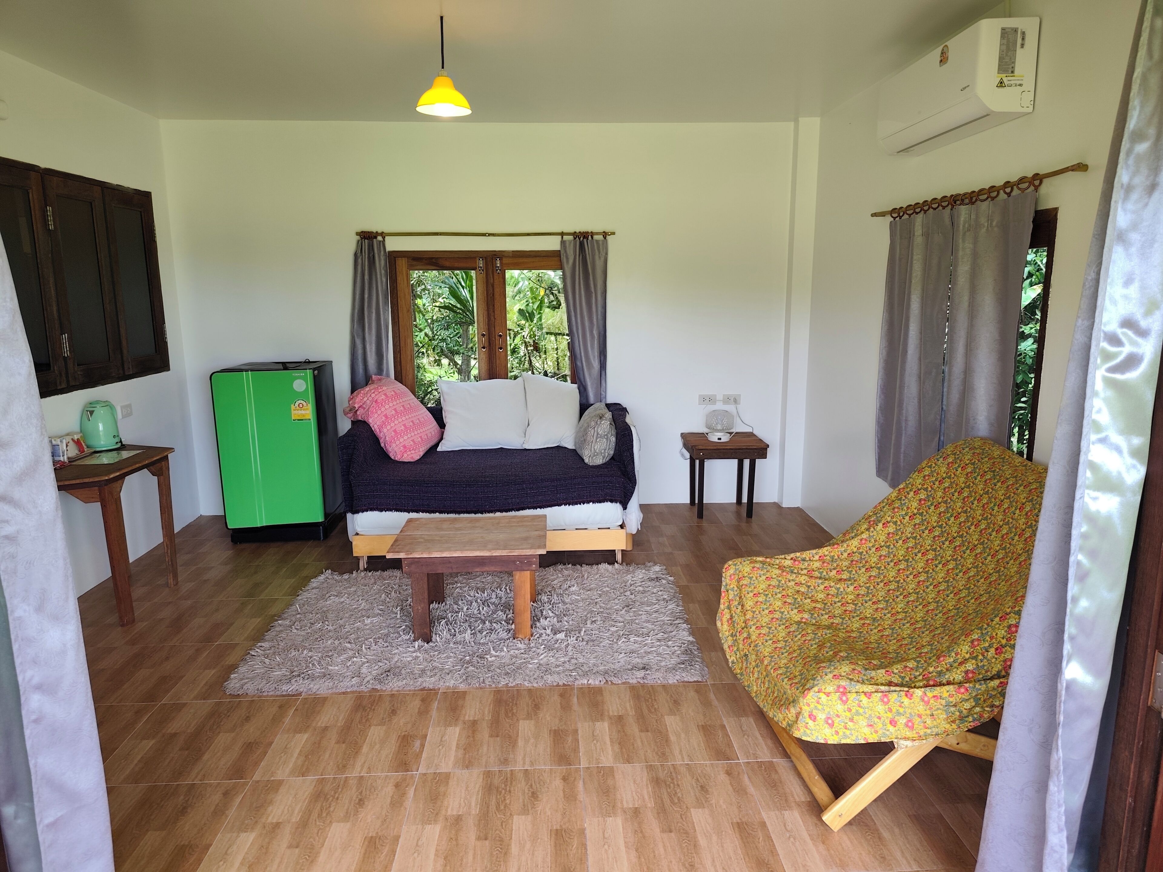 Een gezellige woonkamer met een bank, een groene koelkast, een houten salontafel en een fauteuil met bloemenprint.