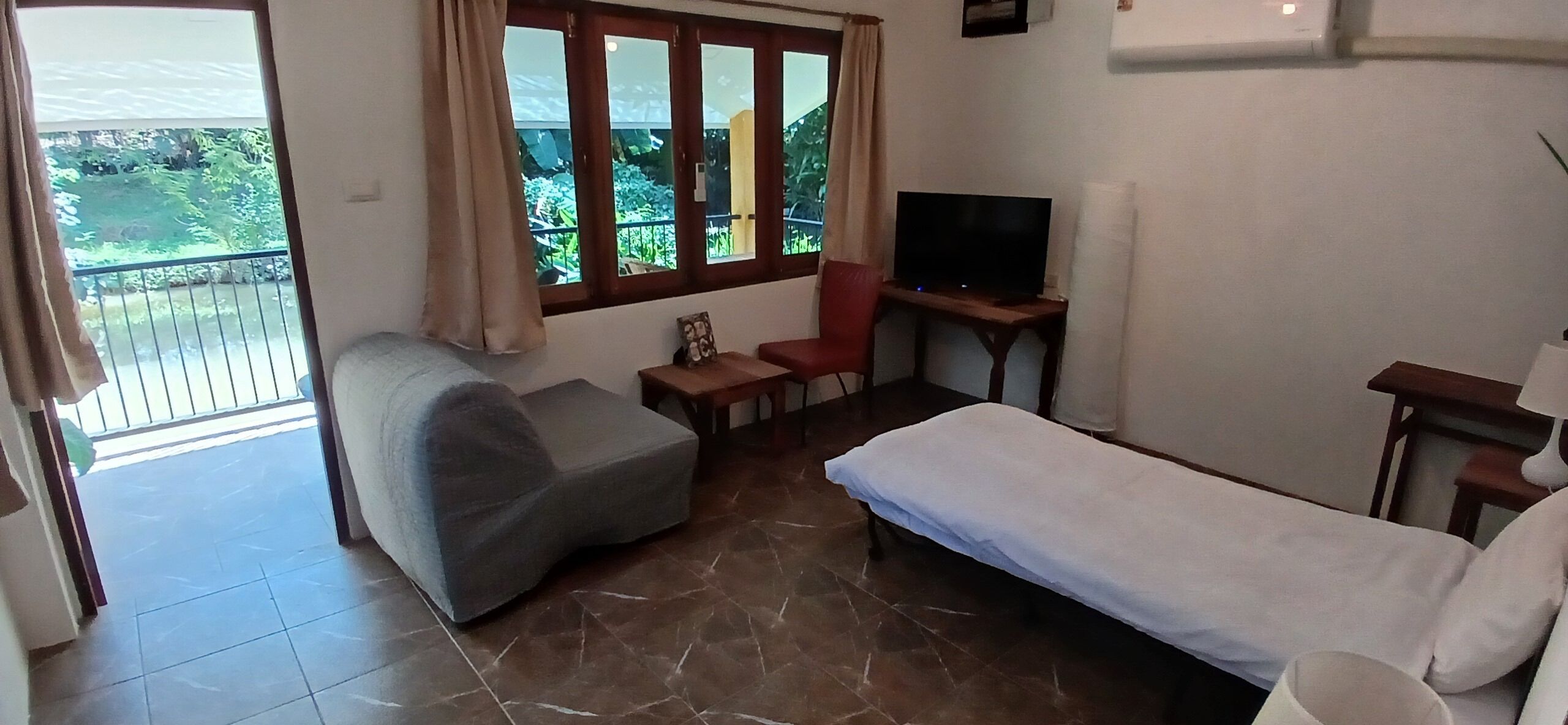 Una habitación con cama, sofá, televisión y una mesita. Tiene un balcón con vistas a zonas verdes.