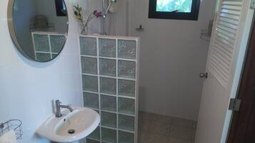 Un baño con lavamanos blanco, un espejo, ducha y ventana con vista a la vegetación.