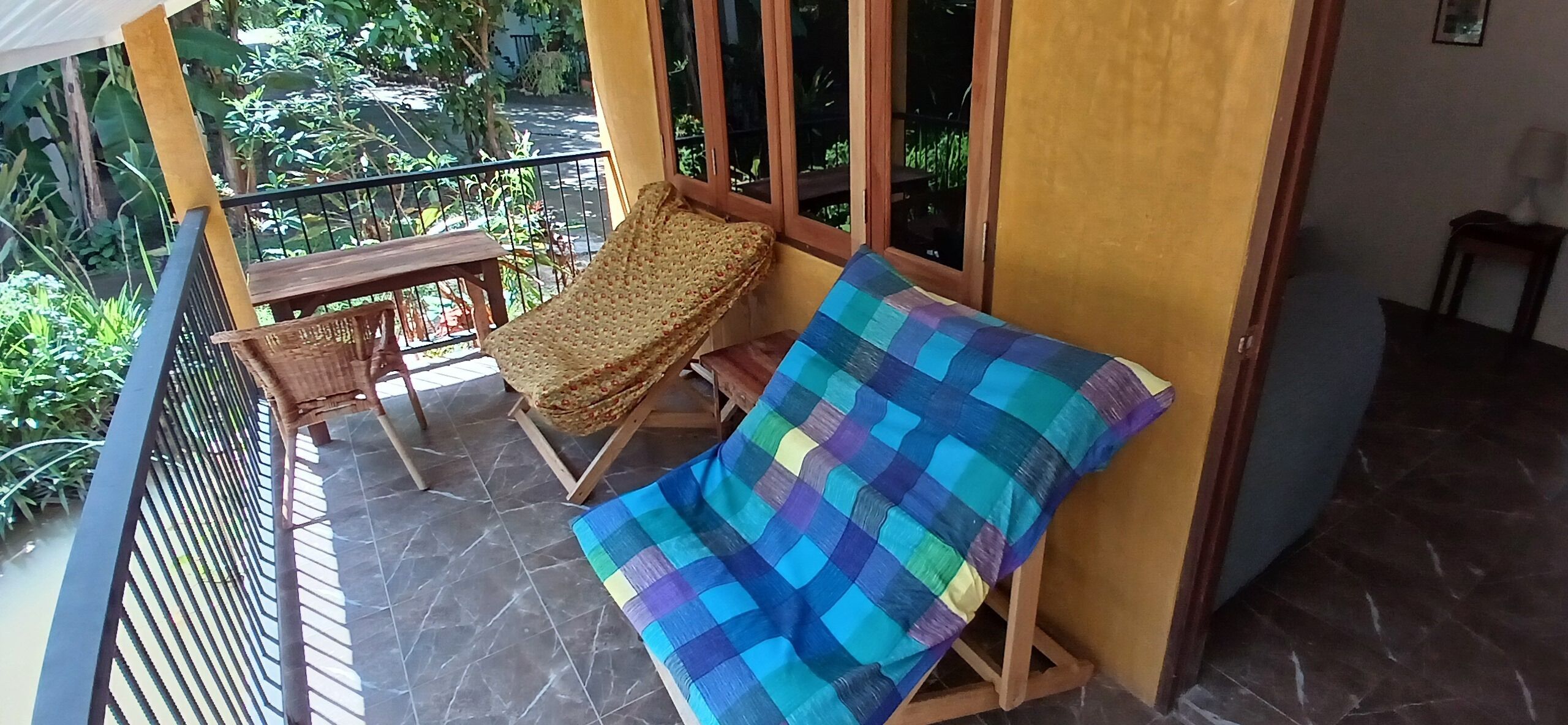 Uma varanda com uma cadeira de vime, uma manta xadrez e uma mesa pequena.
