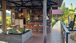 A rustic outdoor bar area with wooden furniture, a seating area with cushions, and a dog resting nearby. - Country Retreat (Mae Rim)