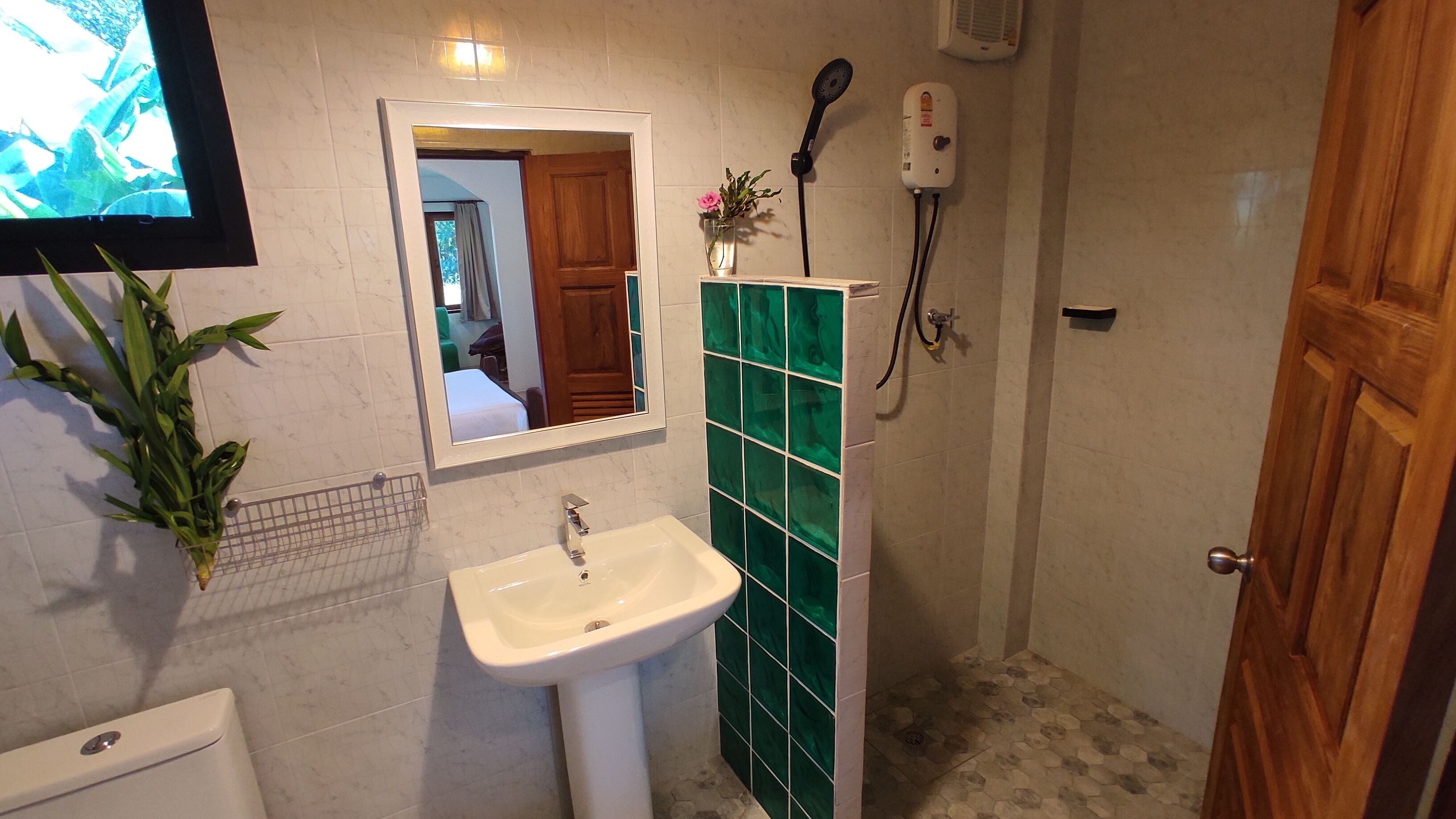 A bathroom with a sink, mirror, and green-tiled shower wall.