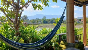 A hammock under a bamboo structure with a view of a rice field and mountains in the background. - Country Retreat (Mae Rim)