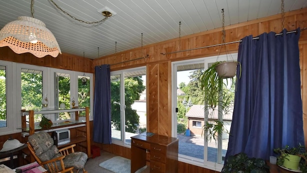 A cozy room with wooden walls, a large window with blue curtains, a wooden desk, and a rocking chair. - 10th Avenue Guest House & Suites (Hanover)